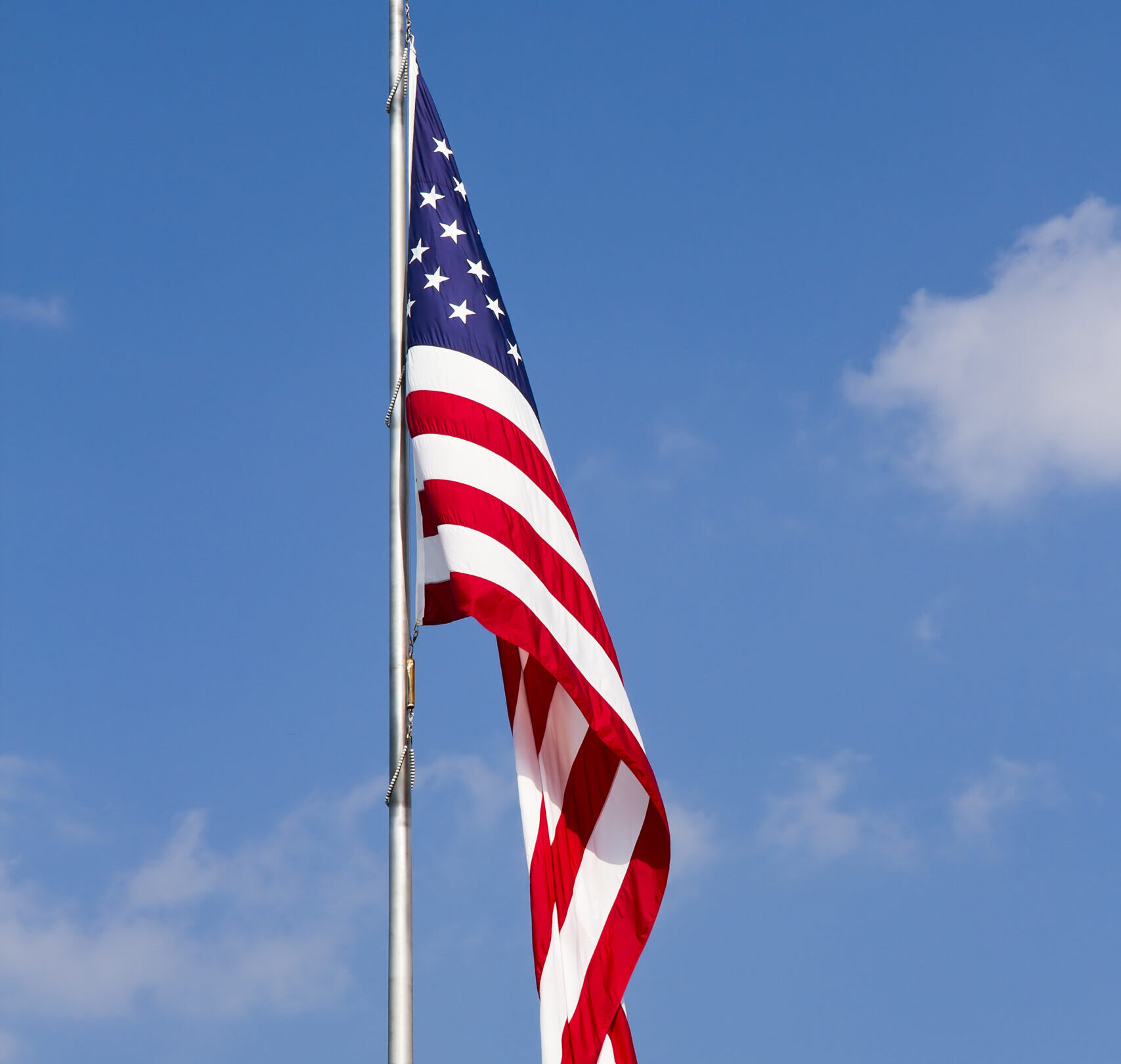 Us,Flag,Waving,On,Pole,Against,A,Blue,,Cloud-draped,Sky.